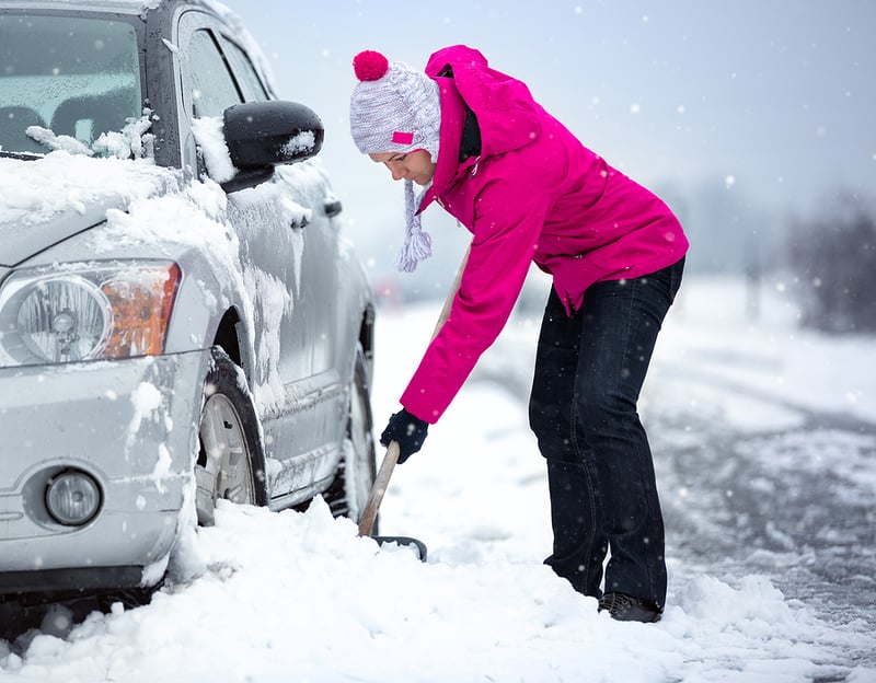 Woman shoveling snow around car